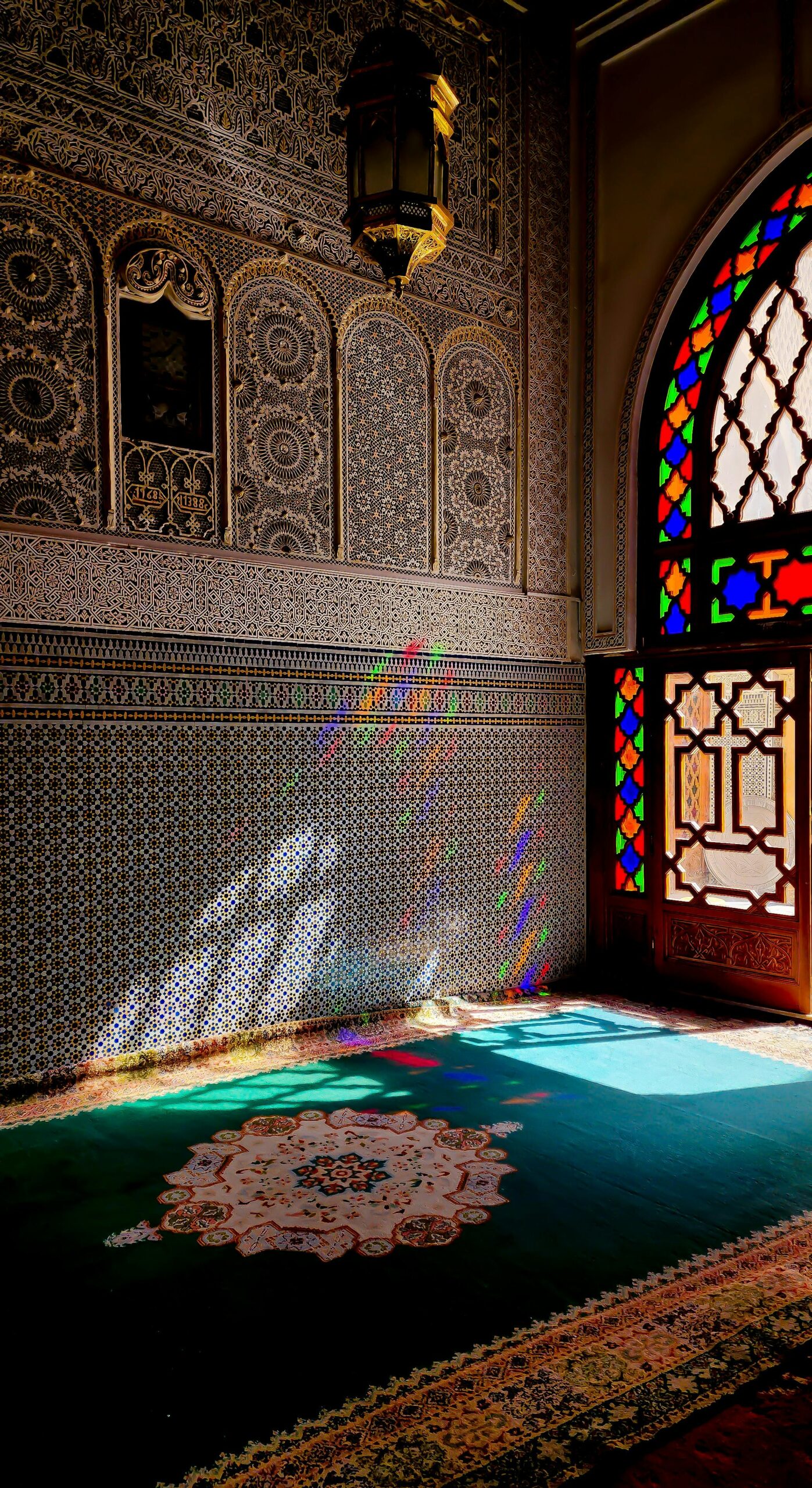 Colorful stained glass window casting rainbow light on ornate Moroccan mosque interior.