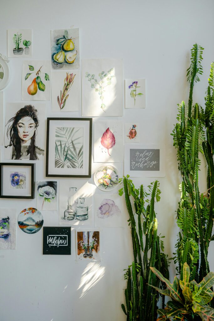 A curated collection of framed illustrations and paintings on a bright wall with indoor plants.